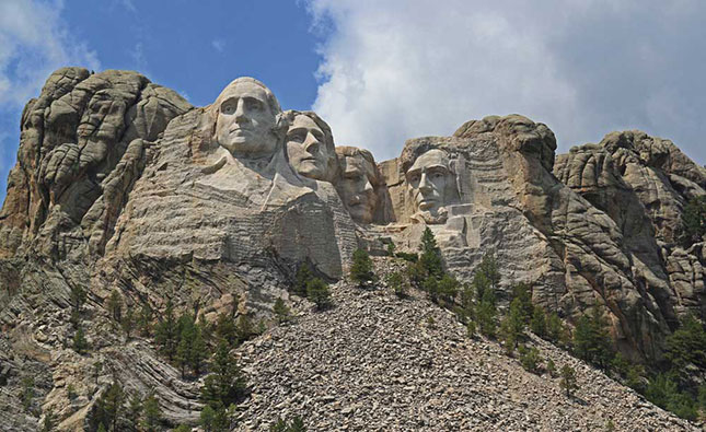 MEGGYALÁZOTT SZENT HEGYEK – Az Egyesült Államokban a Black Hills szikláiba vájt négy elnök (Washington, Jefferson, Roosevelt, Lincoln) arcképe nemzeti szimbólumnak számít. Egykor Thunkásila Sákpeként (Hat Ős) ismerték a sziúk e szent hegyet, később a Mount Rushmore nevet kapta. 1927—1941 közt készültek a hatalmas szobrok, melyek a sziúk számára a fehér ember arroganciáját jelképezik. A Black Hills bolygatásáért a bíróság végül 106 millió dollár kártérítést ítélt meg a sziúknak, de a pénzt sosem vették fel. A Hé-szápa nem eladó. Fotó: Mari László